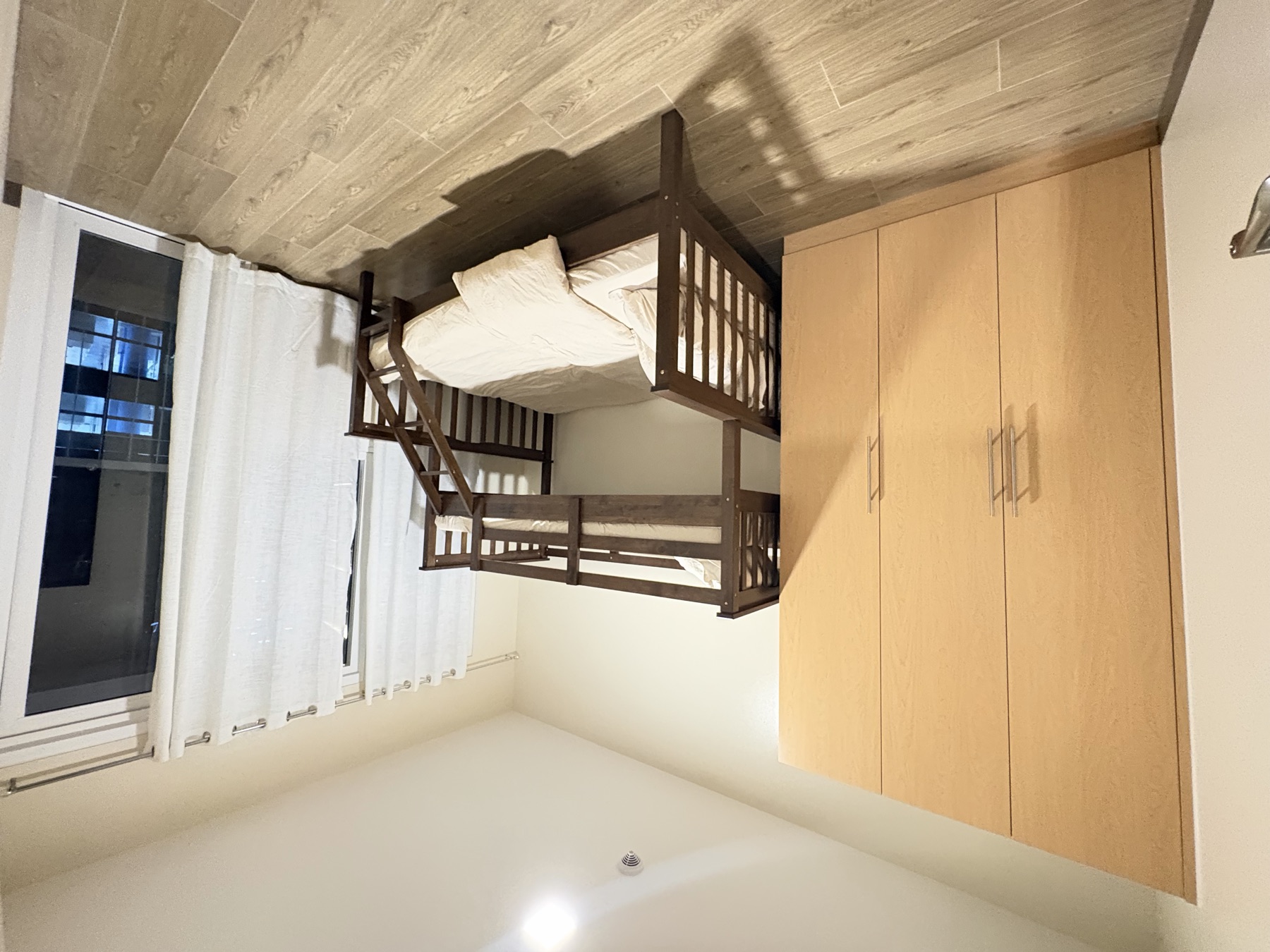 Second bedroom of the DAYON TA condo, with a bunk bed — a double below and a single above — a full-height wardrobe, and a balcony door onto the city
